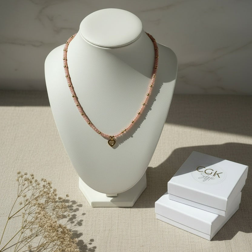 Collar CGK Style de cuentas rosa pastel con dije de corazón dorado sobre busto expositor y cajas de regalo
