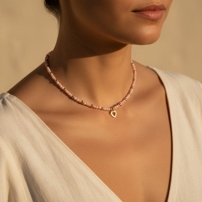 Collar CGK Style de cuentas rosa pastel y detalles dorados con un dije de corazón puesto en el cuello de una mujer
